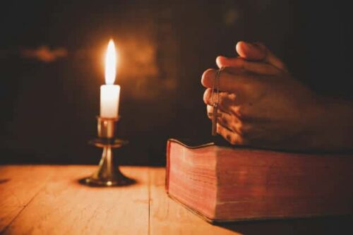 close up da mao do homem esta rezando na igreja com vela acesa