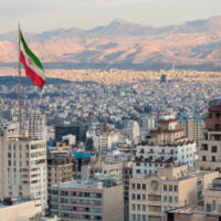 Waving Iran flag above skyline of Tehran at sunset.